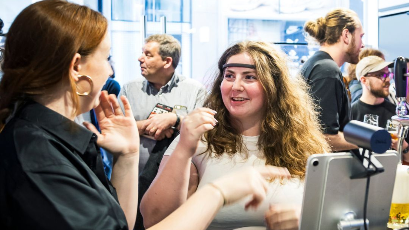 two women are laughing together. One is wearing a EEG headset and the other is pointing to an ipad two women are laughing together. One is wearing a EEG headset and the other is pointing to an ipad